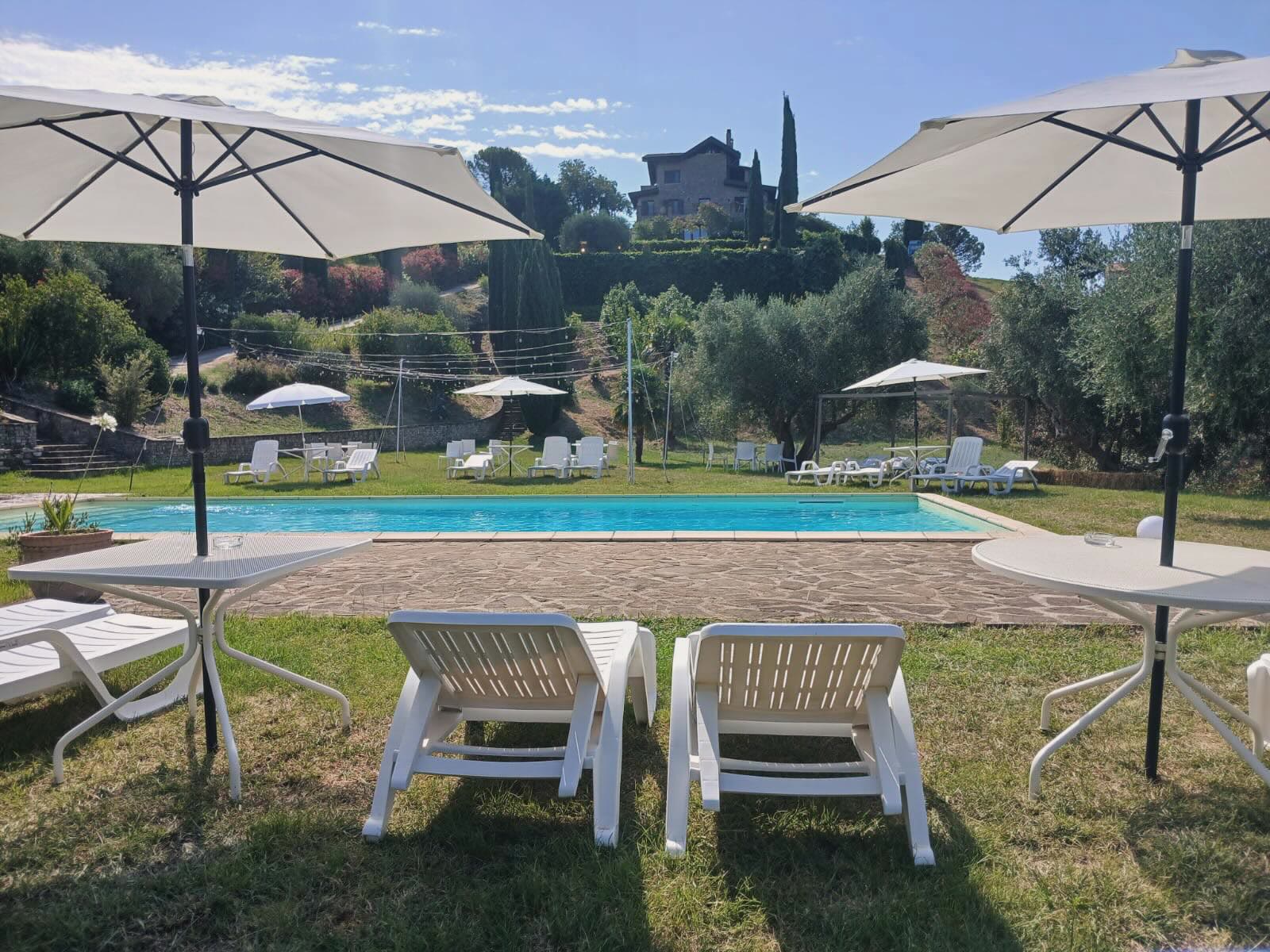 La piscina della tenuta con il casale sulla collina, tra ulivi e cipressi