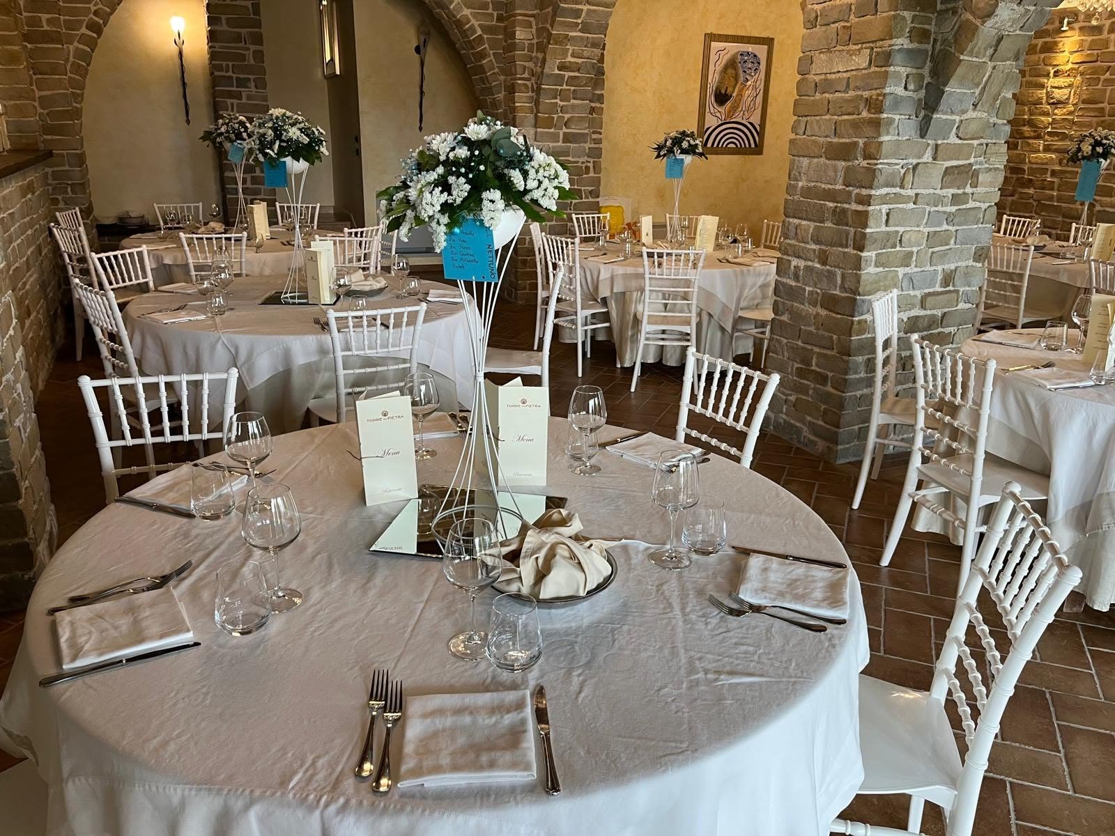 Sala con archi in pietra allestita per una cerimonia, con composizioni di fiori bianchi